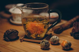 A glass cup of chrysanthemum tea with blooming flower steeped in warm water on a wooden table.