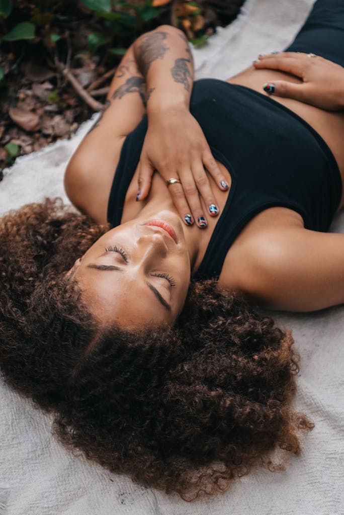 A relaxed woman with curly hair napping on a blanket outdoors, exuding tranquility.