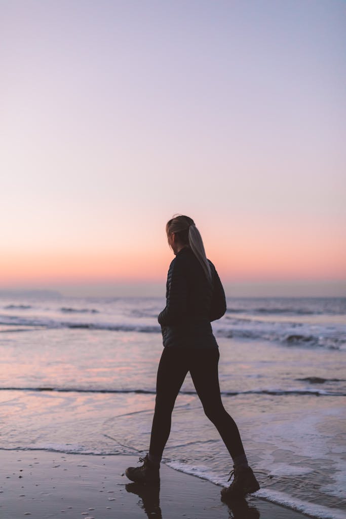 A woman walks along the beach at sunset, enjoying the tranquil ocean scenery.