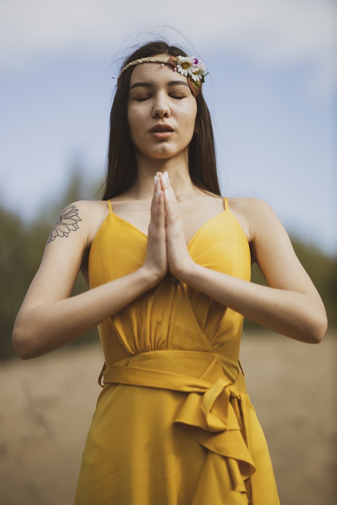 A young woman meditating outdoors in a yellow dress, embracing peace and relaxation.