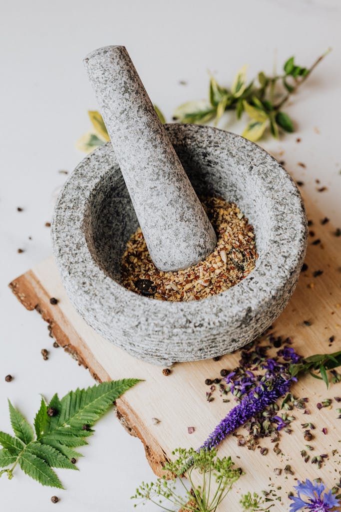 Granite mortar with pestle grinding mixed herbs and spices on a rustic wooden board.