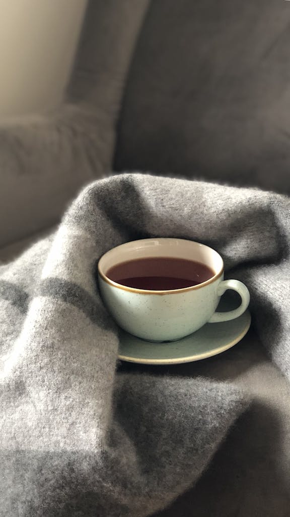 A warm cup of coffee nestled in a soft gray blanket, creating a cozy atmosphere.